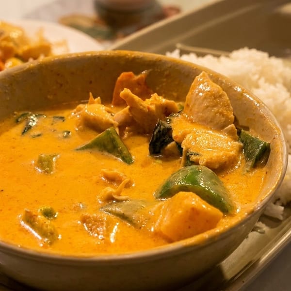 A bowl of orange curry with chicken and green peppers, served with white rice.