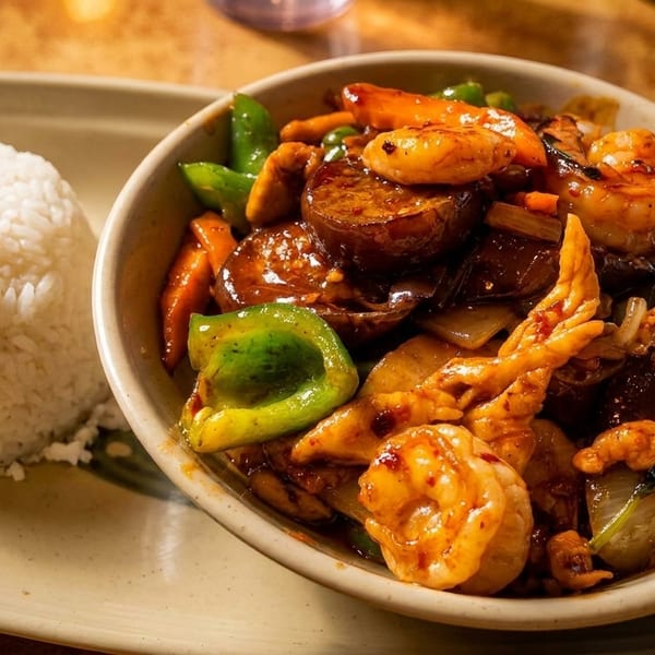 A bowl of stir-fried shrimp, chicken, and vegetables with a side of white rice.
