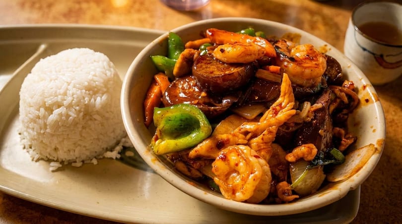 A bowl of stir-fried shrimp, chicken, and vegetables with a side of white rice.