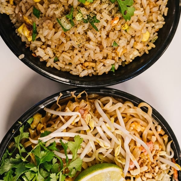 Two black bowls of Asian cuisine, one with fried rice and the other with noodles and bean sprouts.