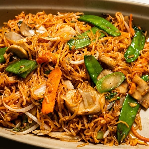 Close-up of a large serving of lo mein noodles with snow peas, mushrooms, and carrots.